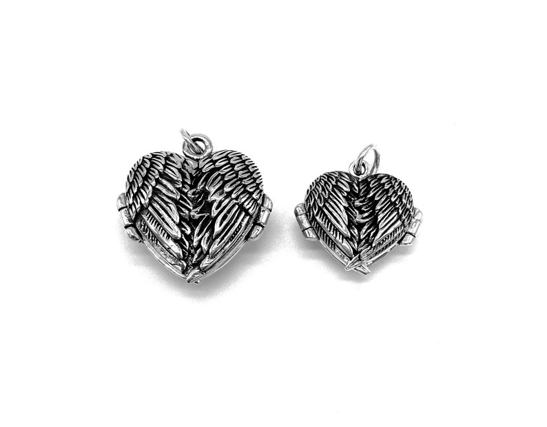 May include: Two silver heart-shaped lockets with angel wings. The lockets are open and the wings are spread out. The larger locket is on the left and the smaller locket is on the right.