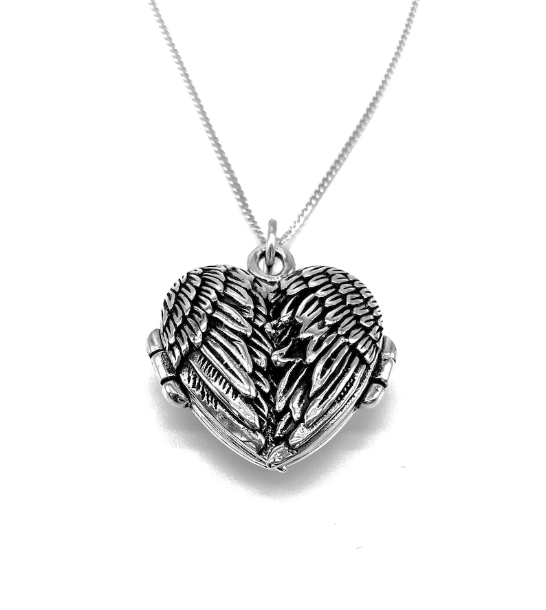 May include: A silver heart-shaped locket with angel wings on the front. The locket is on a silver chain.