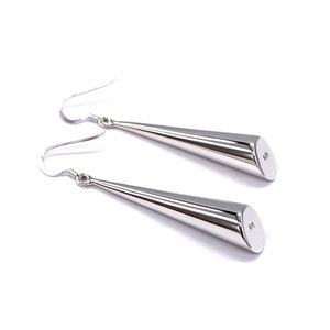 May include: A pair of silver-colored, cone-shaped earrings with a hook closure. The earrings are smooth and polished, with a rounded end. The earrings are displayed on a white background.