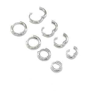May include: A set of eight silver hoop earrings of varying sizes. The hoops are all made of a thick, rounded wire.