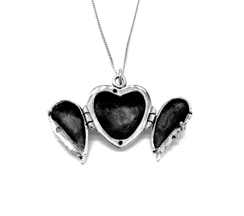 May include: Silver heart-shaped locket necklace with two open wings. The locket is open, revealing the empty interior.