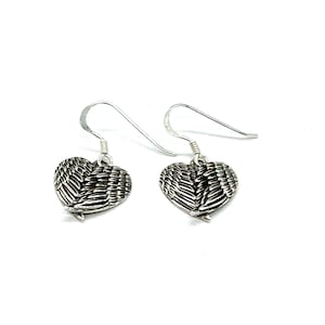 May include: Silver dangle earrings with a heart-shaped charm featuring a detailed design of angel wings.