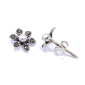 May include: A pair of silver flower stud earrings with a pearl centre and marcasite accents.