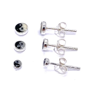 Op de afbeelding: Drie paar zilveren oorbelletjes met zwarte en witte yin yang symbolen. De oorbelletjes zijn klein en delicaat.