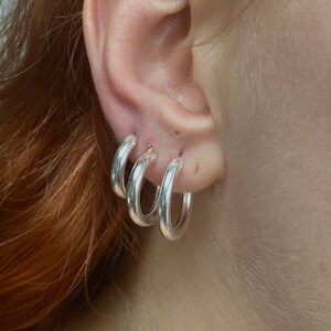 May include: Three silver hoop earrings of different sizes, worn in a person's ear.