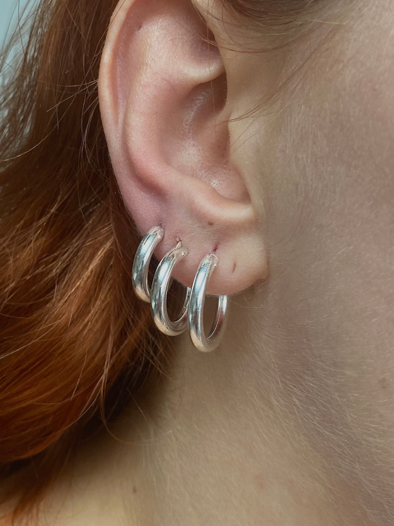 May include: Three silver hoop earrings of different sizes, worn in a person's ear.