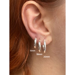 May include: Three silver hoop earrings in different sizes, 15mm, 18mm, and 20mm, shown on a person's ear.