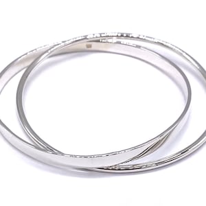May include: Two silver bangle bracelets, one slightly wider than the other, are stacked on top of each other.