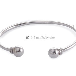 May include: A silver bangle bracelet with two round balls on the ends. The bracelet is 2 mm wide and has a diameter of 45 mm. The bracelet is labelled "baby size".