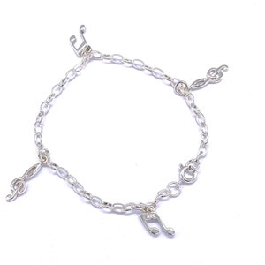 May include: Silver charm bracelet featuring four music note charms. The bracelet is made from a silver chain and has a lobster clasp fastening.