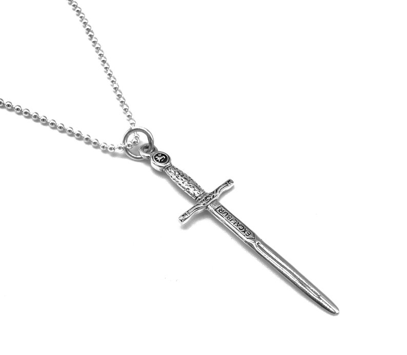 May include: A silver necklace with a sword pendant. The sword has the word "Excalibur" inscribed on it.