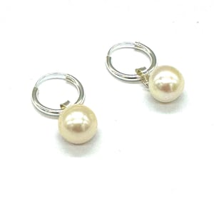 May include: A pair of silver hoop earrings with a single white pearl dangling from each hoop.