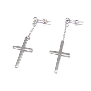 May include: A pair of silver dangle earrings with a cross charm hanging from a chain. The earrings have a simple, minimalist design.