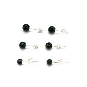 May include: A set of six black onyx stud earrings with silver posts. The earrings are round and have a smooth, polished finish.