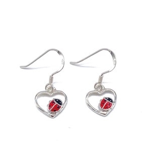 May include: Silver heart-shaped earrings with a red and black ladybug charm inside each heart.