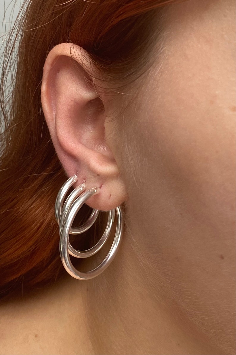 May include: Three silver hoop earrings of different sizes worn in one ear.