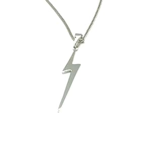 Op de afbeelding: Een zilverkleurige ketting met een bliksemvormige hanger. De hanger heeft een gestileerde, langwerpige zigzagvorm en hangt aan een fijne ketting. De ketting wordt getoond tegen een witte achtergrond.