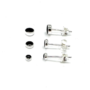 May include: Three pairs of silver stud earrings with black round stones. The earrings are different sizes.