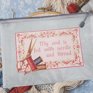 May include: A light blue mesh craft bag with a printed design that reads "My soul is fed with needle and thread." The design includes scissors, spools of thread, and floral accents. A wooden embroidery hoop is visible in the background.