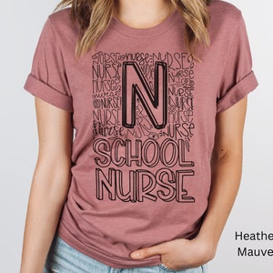 May include: A heather mauve t-shirt with a black graphic design that says "School Nurse" with the letter "N" made up of the word "Nurse" repeated multiple times.