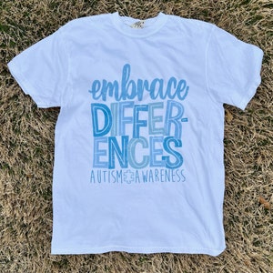 May include: White t-shirt with a blue and white graphic that says "embrace differences" and "autism awareness".