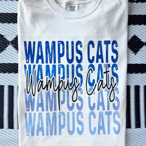 May include: A white t-shirt with a blue and white ombre design that says "Wampus Cats" repeated five times.