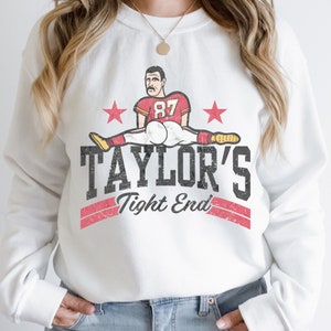 May include: White sweatshirt with a vintage-style graphic of a football player in a red and white uniform. The graphic says "TAYLOR'S Tight End" with a red and white stripe design.