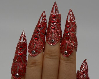 May include: Five red metal claw rings with rhinestones. The rings are worn on a hand, with each ring on a different finger.