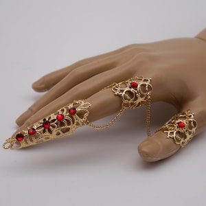 Könnte beinhalten: Goldener Filigranring-Set mit roten Edelsteinen. Die Ringe sind durch eine Kette verbunden und können an mehreren Fingern getragen werden.