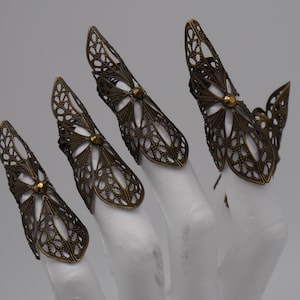 Könnte beinhalten: Vier goldfarbene Filigran-Fingerringe mit Blumenmuster. Die Ringe werden an einer weißen Mannequin-Hand getragen.