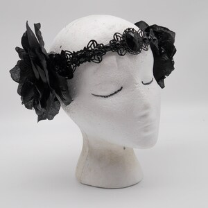 May include: Black lace headband with a large black gemstone and two black fabric roses on either side.