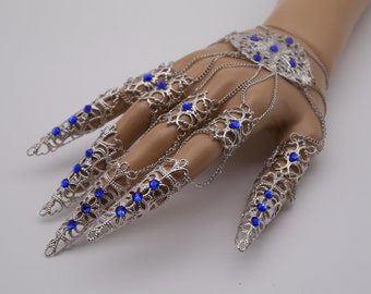 May include: Silver finger rings with blue rhinestones, designed to be worn on multiple fingers, connected by chains.