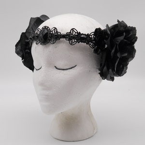 May include: Black lace headband with a large black gemstone and black fabric roses on either side.