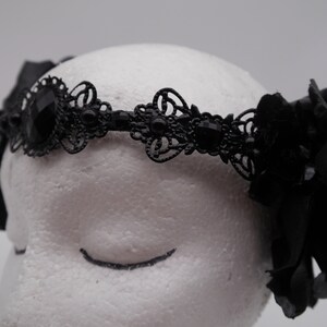 May include: Black lace headband with a large black flower on each side. The headband is decorated with black rhinestones.