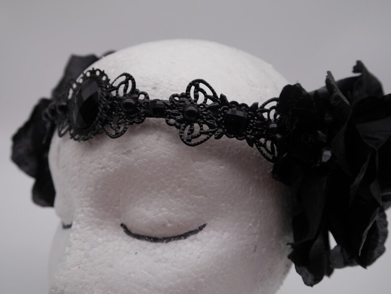 May include: Black lace headband with a large black flower on each side. The headband is decorated with black rhinestones.
