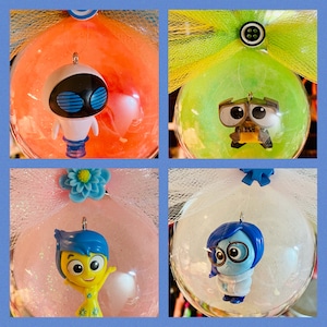 May include: Four glass ornaments with different characters from the Pixar movie Inside Out. The ornaments are decorated with tulle and glitter. The characters include Joy, Sadness, Wall-E, and Eve.