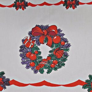 Könnte beinhalten: Ein weißer Stoff mit einem sich wiederholenden Weihnachtskranzmuster. Der zentrale Kranz besteht aus grünen Tannennadeln, violetten Akzenten, roten Schleifen, roten Kugeln, einem verpackten Geschenk und einem Bonbon. Ein roter Wellenrand verläuft entlang der Kanten.