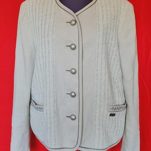 May include: A light beige jacket featuring a round neckline, long sleeves, and a front button closure with five silver-toned metal buttons. The garment includes vertical textured panels on the front, two pockets with embroidered leaf details, and dark piping trim.