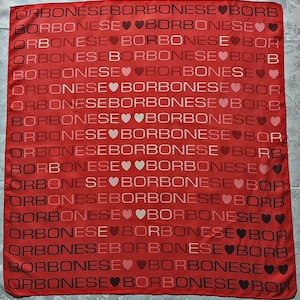 May include: A square red scarf featuring a repeating pattern of the word BORBONESE printed in black and white letters, interspersed with small heart icons in varying shades of pink, red, and white across the entire fabric surface.