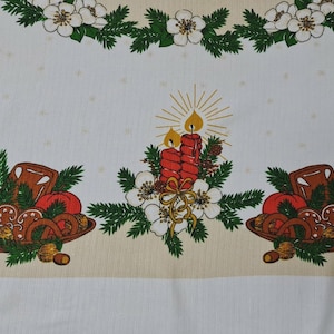 Könnte beinhalten: Eine weiße Tischdecke mit einem wiederkehrenden Weihnachtsmuster aus roten Kerzen mit gelben Flammen, grünen Tannenzweigen, weißen Blüten und braunen Schalen mit roten Äpfeln, Brezeln und Walnüssen auf einem hellbeigen Rand.