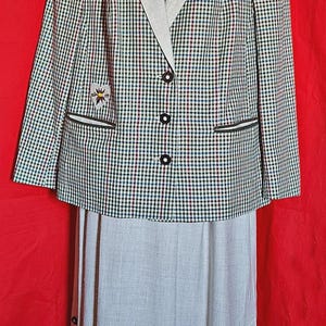 May include: A two-piece outfit consisting of a blazer and a skirt. The blazer features a multi-coloured checkered pattern, a light beige lapel, three dark buttons, and a small heart-shaped patch. The skirt is light beige with side buttons.