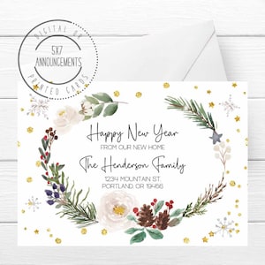 May include: A white announcement card with a floral wreath design. The card reads "Happy New Year From Our New Home The Henderson Family" with an address below. The card is 5x7 inches and includes gold glitter accents and snowflakes.