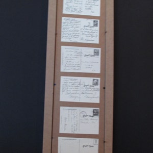 May include: A wooden frame with six postcards inside. The postcards are all different sizes and have handwritten messages on them. The frame is hanging on a black wall.
