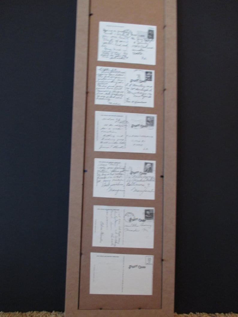 May include: A wooden frame with six postcards inside. The postcards are all different sizes and have handwritten messages on them. The frame is hanging on a black wall.