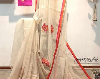 May include: Off-white saree with a striped pattern, featuring embroidered floral designs in shades of orange and pink. The saree has a bright pink border with orange trim. A matching pink fabric with floral embroidery is also displayed.