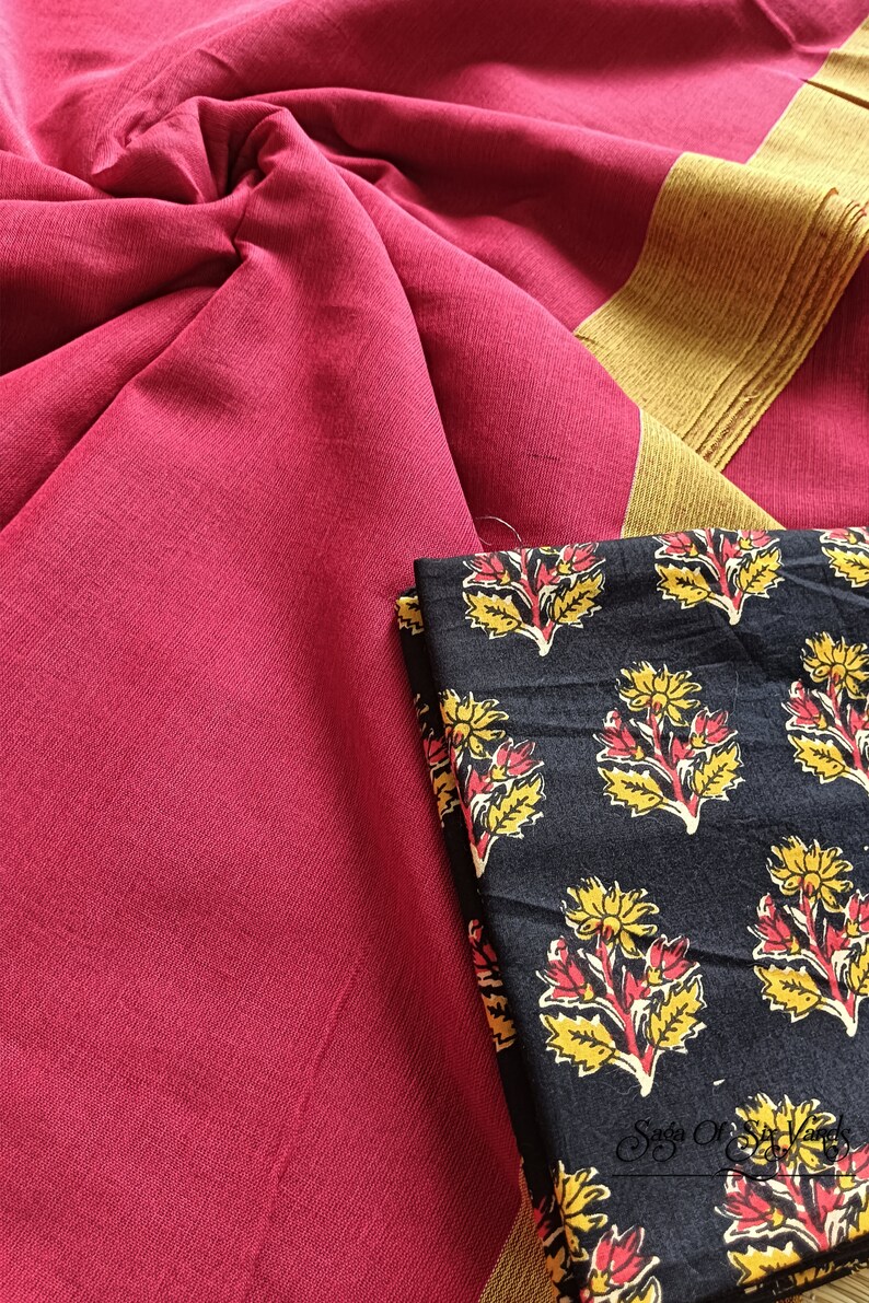 May include: A close-up of a textile arrangement featuring a deep red fabric with a gold border. A folded black fabric with a floral pattern in yellow and red is also visible. The textile is likely used for clothing or home decor.
