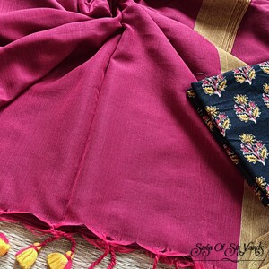 May include: A magenta-colored textile with a scalloped edge and yellow and pink tassels. A black fabric with a floral pattern is visible. The textile has a gold border. The overall theme is a traditional garment.