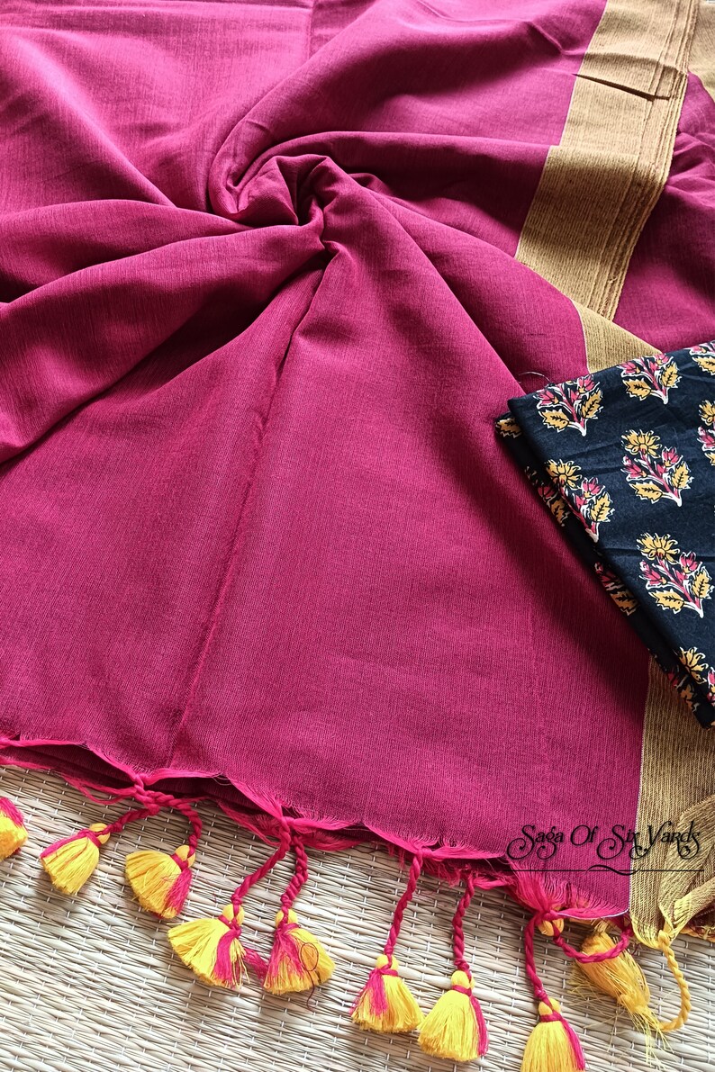 May include: A magenta-colored textile with a scalloped edge and yellow and pink tassels. A black fabric with a floral pattern is visible. The textile has a gold border. The overall theme is a traditional garment.