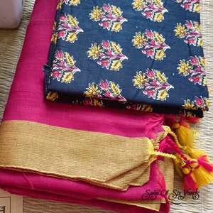 May include: A vibrant pink fabric with a gold border is folded neatly, topped with a navy blue patterned fabric. The navy fabric features a repeating floral design in yellow and red. Yellow and pink tassels are visible.