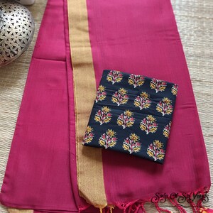May include: A magenta textile with a gold border and tassels. A black square fabric with a floral pattern in yellow, red, and white rests on top. The text "Saga Of Six Yards" is visible in the bottom right corner.